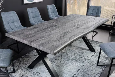 A modern dining table with a rustic gray wood top and black metal legs, set with chairs on a patterned rug.