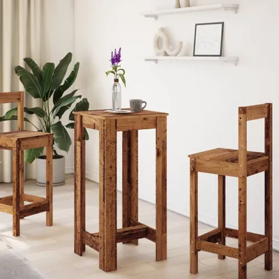 A wooden bar table and two bar stools are set up in a room with a large potted plant and shelves on the wall.