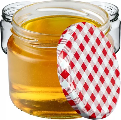 A close-up shot of a glass jar filled with honey, with a red and white checkered lid partially covering it. Other empty jars are visible in the background.