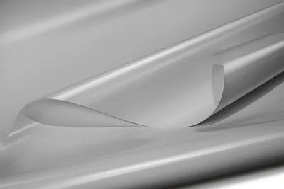 A close-up shot of a gray PVC tarpaulin material, rolled and curved, showcasing its texture and sheen.