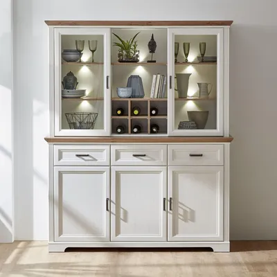 A white and wood-toned buffet with glass doors and internal lighting, displaying various decorative items and wine bottles.