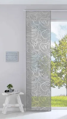 A panel curtain with a white abstract pattern hangs in front of a window with a view of a tree and grass. A small white stool with a plant and some papers sits to the left of the curtain.