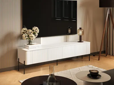 A modern living room scene featuring a white TV lowboard with fluted doors, a large black television, and decorative elements.