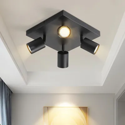 A black ceiling light fixture with four adjustable spotlights is mounted on a white ceiling.