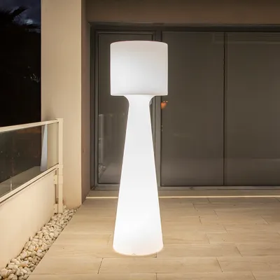 A tall, white, illuminated outdoor floor lamp stands on a tiled patio at night.