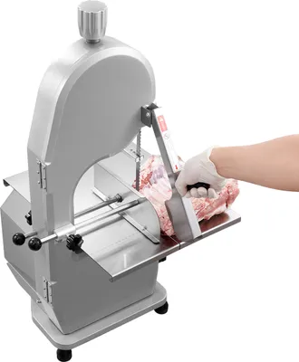 A person wearing a white glove is using a commercial electric meat band saw to cut a piece of meat.