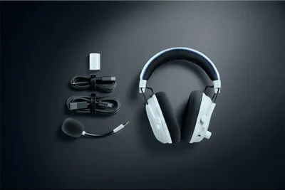 A pair of white and black gaming headphones with accessories laid out on a dark background.