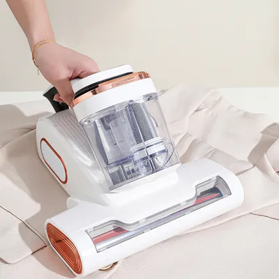 A hand is holding a white and copper handheld vacuum cleaner over a light-colored garment.