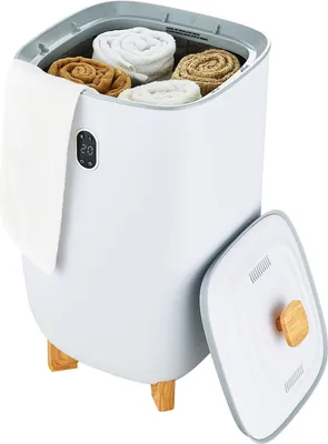 A white towel warmer bucket with rolled towels inside, a white towel hanging from the side, and the lid open to the side. The bucket has wooden legs and a digital display.