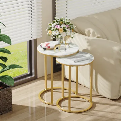 Two nesting round side tables with marble-look tops and gold metal frames are placed next to a sofa, with a bouquet of flowers on the larger table.