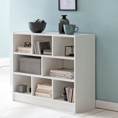 A white bookshelf filled with various items like books, CDs, and decorative objects, set against a light blue wall.