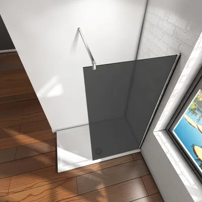 A modern shower enclosure with a smoked glass panel and a white base, set against a white wall and a brick wall, with wooden flooring.