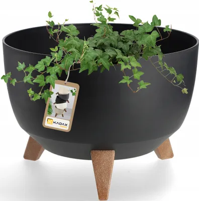 A black planter with three wooden legs and a plant growing out of it. A tag is hanging from the planter.
