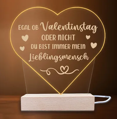 A heart-shaped LED lamp with a German inscription, placed on a wooden base.