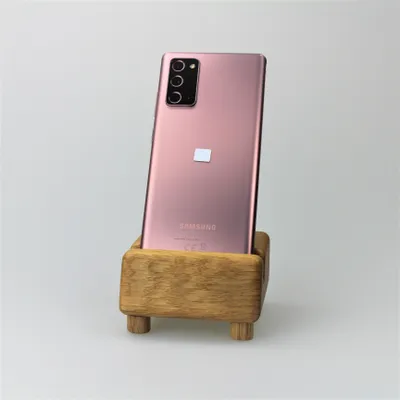 A pink Samsung Galaxy Note20 5G smartphone is displayed in a wooden stand against a white background.