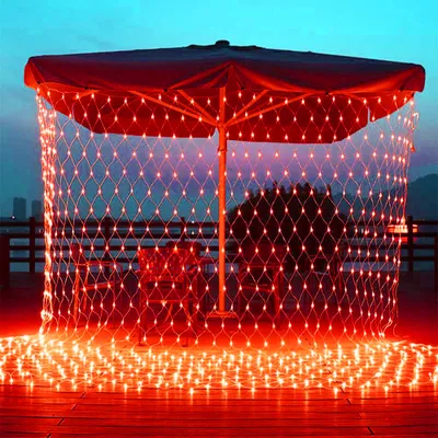 Red net lights are draped over an outdoor umbrella and illuminate a wooden deck at dusk.