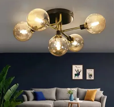 A modern living room with a sectional sofa, plants, and artwork on the wall, illuminated by a ceiling light.
