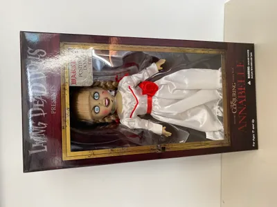 A doll in its packaging, displayed on a white and light gray surface.
