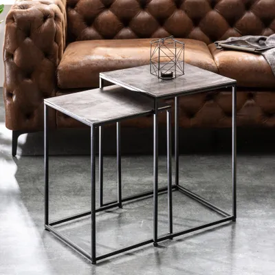 A set of nesting side tables with a metal frame and stone-like tops, placed in front of a tufted leather sofa.