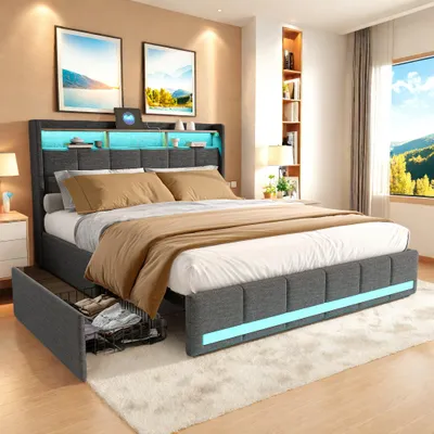 A modern bedroom with a grey upholstered bed frame featuring integrated LED lighting and storage. The bed is made up with white and brown linens, and two framed pictures hang on the wall above the headboard. A window with a scenic view is visible on the ri