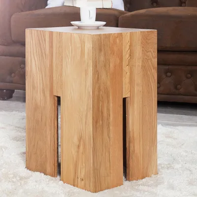 A wooden side table with a cup and saucer on top, placed on a rug next to a brown sofa.