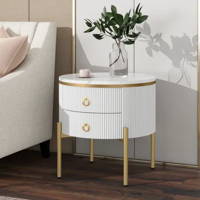 A white round side table with gold legs and drawer pulls, next to a sofa.