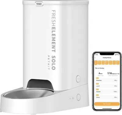 A white automatic pet feeder is shown next to a smartphone displaying a feeding schedule app.