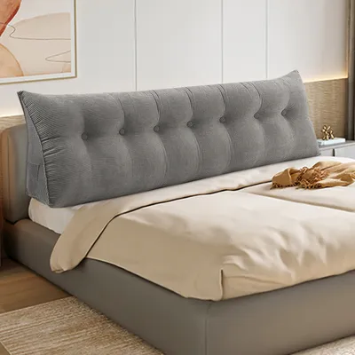 A grey tufted wedge pillow is placed on a bed behind the pillows.