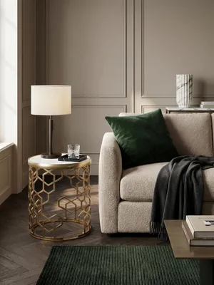 Draufsicht auf den runden Marmor-Beistelltisch neben einer Couch, der das goldene geometrische Metallgestell und die Tischdeko aus Tasse und Figur zeigt._#sku_SAFWL6.629#