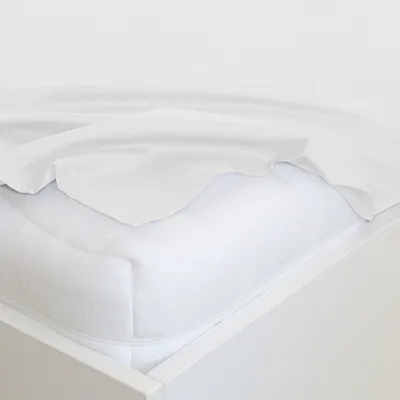 A white bed sheet is draped over a white mattress protector on a bed frame.