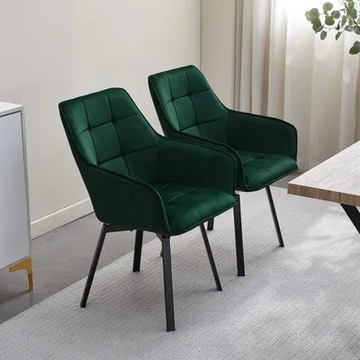 Two green velvet dining chairs are shown in a room with a light-colored rug and a table.