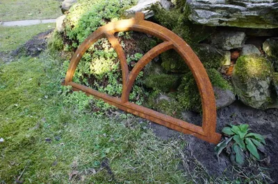 A rusty metal window frame lying on the ground next to a stone wall and mossy vegetation.