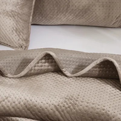A close-up view of a beige quilted blanket folded on a bed.