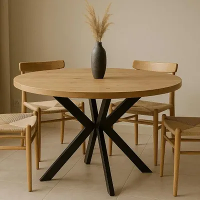 A round wooden dining table with black metal legs, surrounded by four chairs, in a well-lit room.