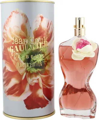 Parfumflakon in Form eines Frauenkörpers mit Blume am Hals, daneben zylindrische Dose mit Blütenmotiv und goldener Schrift „La Belle Flower Edition“.