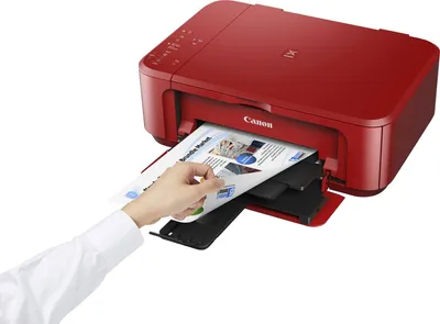 A red Canon PIXMA MG3650S printer is shown with a hand inserting paper into the output tray.