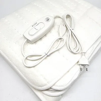 A white electric blanket with a controller and power cord is laid out on a white surface.