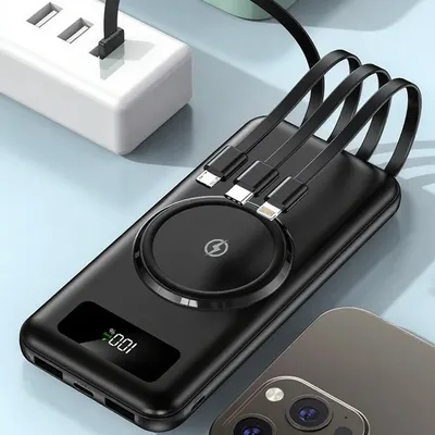 A black wireless power bank with integrated cables is shown connected to a white power strip, with a smartphone partially visible in the foreground.
