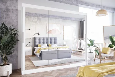 A bedroom scene reflected in mirrored closet doors, showing a bed, nightstand, and plants.