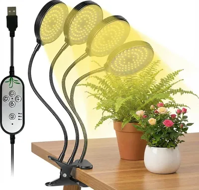 A clip-on LED grow light illuminating two potted plants on a wooden desk.