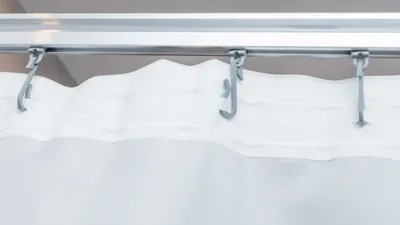 A close-up view of a white fabric shower curtain hanging from a metal track with hooks.