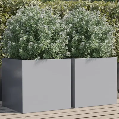 Two silver planters filled with green plants on a wooden deck, with a green hedge in the background.