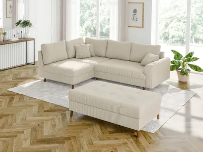 A modern living room with a beige sectional sofa and ottoman, set against a backdrop of large windows and wooden flooring.