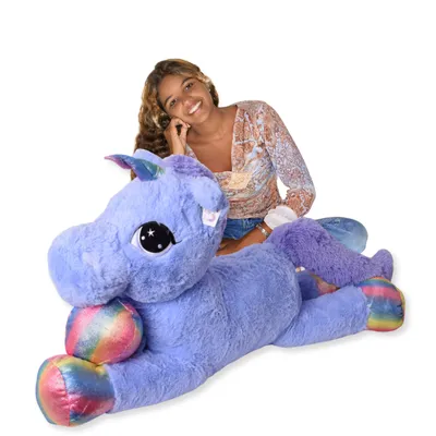 A young woman is sitting behind a large plush unicorn toy.
