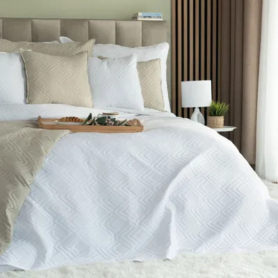 A neatly made bed with a white quilted bedspread, decorative pillows, and a throw blanket.