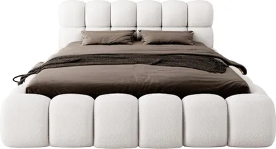 A white upholstered bed with brown bedding and a dark throw blanket.