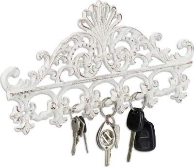 A white, ornate key holder with keys hanging from it.