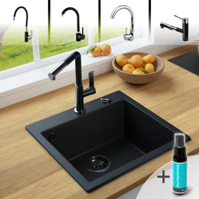 A black granite kitchen sink with a faucet, set on a wooden countertop, with oranges in a bowl and other faucets visible in the background through a window.