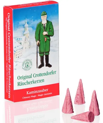 Auf dem Bild ist eine Packung Original Crottendorfer Räucherkerzen mit der Aufschrift Kaminzauber zu sehen die vier rosafarbene Räucherkerzen in Kegelform zeigt und im Hintergrund eine winterliche Illustration eines Mannes vor einem Dorf hat