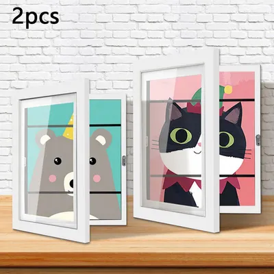 Two open white frames displaying cartoon animal artwork, placed on a wooden surface against a white brick wall.